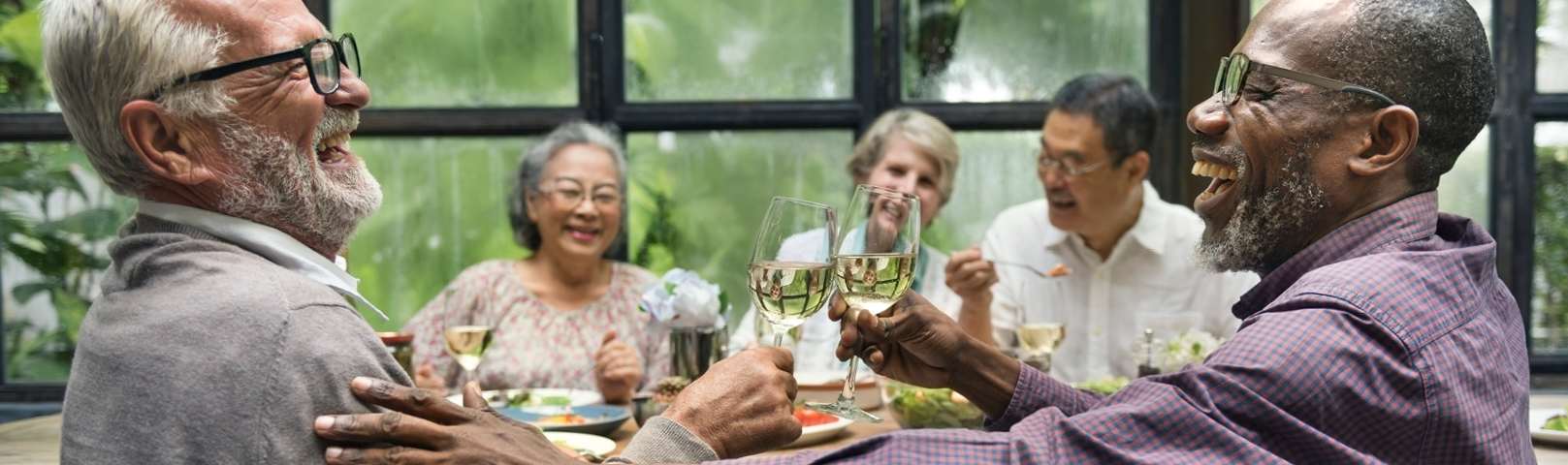 an african american man laughs deeply as he enjoys a friendly meal with neighbors and friends without fear of hearing loss interrupting the good time